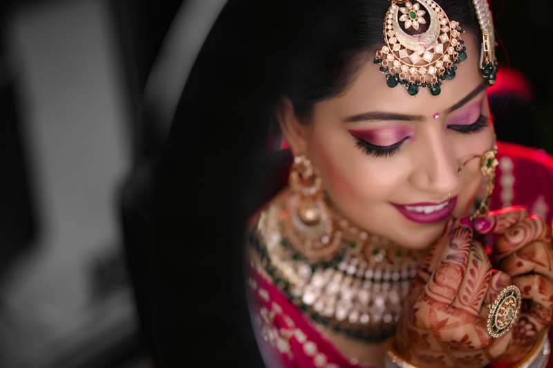 Bride applying soft pink lipstick with ring-adorned hand in natural light